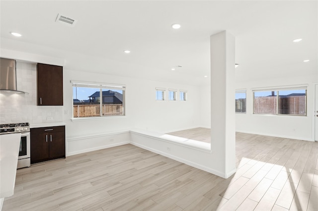 kitchen with wall chimney exhaust hood, gas stove, dark brown cabinets, and light wood-type flooring