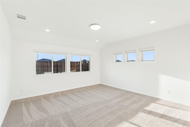 empty room with a wealth of natural light, lofted ceiling, and light colored carpet