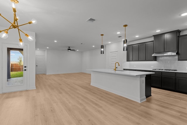 kitchen with a center island with sink, ceiling fan with notable chandelier, sink, light hardwood / wood-style flooring, and decorative light fixtures