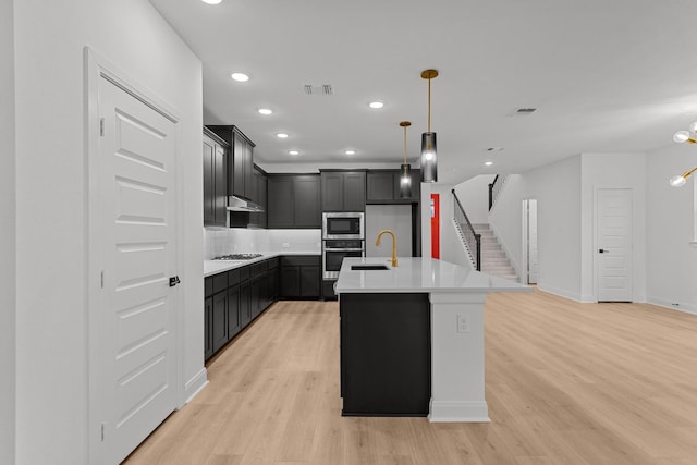 kitchen featuring stainless steel appliances, a center island with sink, light hardwood / wood-style floors, and sink