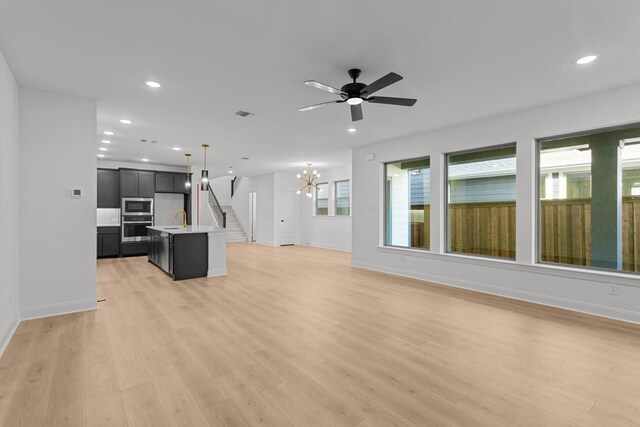 living room with ceiling fan with notable chandelier, sink, and light hardwood / wood-style flooring