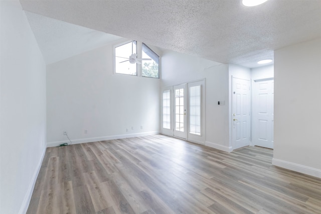 spare room with a textured ceiling, light hardwood / wood-style flooring, french doors, ceiling fan, and vaulted ceiling