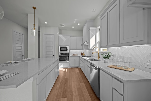 kitchen with appliances with stainless steel finishes, white cabinets, light stone countertops, pendant lighting, and light wood-type flooring