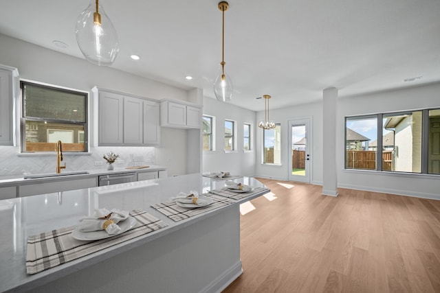 kitchen with decorative backsplash, white cabinets, light wood-type flooring, stainless steel dishwasher, and sink