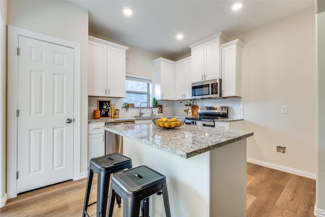 kitchen with light hardwood / wood-style flooring, a breakfast bar area, stainless steel appliances, and white cabinets