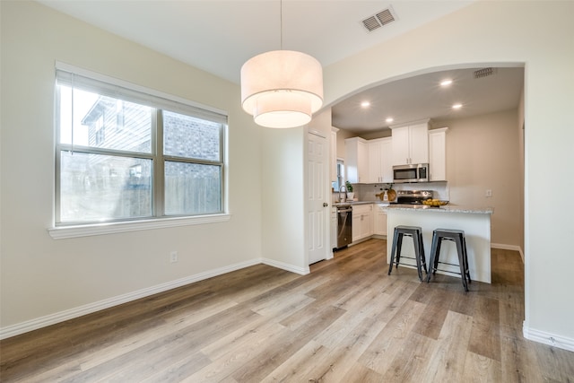 kitchen with light hardwood / wood-style floors, a kitchen bar, stainless steel appliances, white cabinetry, and light stone counters