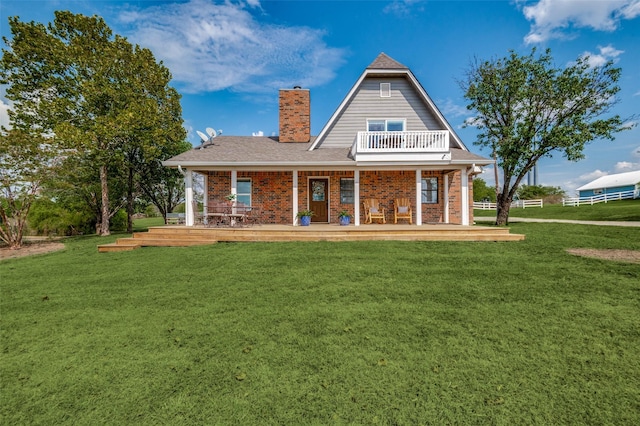 back of house featuring a lawn, covered porch, roof with shingles, brick siding, and a chimney