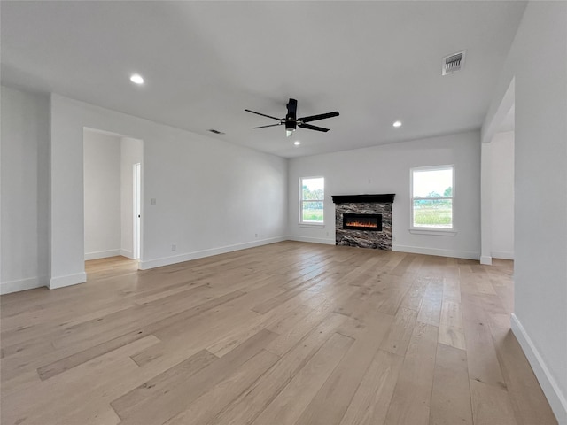 unfurnished living room with a stone fireplace, ceiling fan, and light hardwood / wood-style flooring