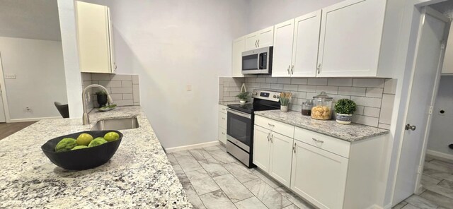 kitchen featuring stainless steel appliances, light stone countertops, sink, and white cabinets