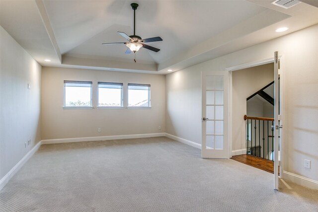 spare room featuring light carpet, a tray ceiling, french doors, and ceiling fan