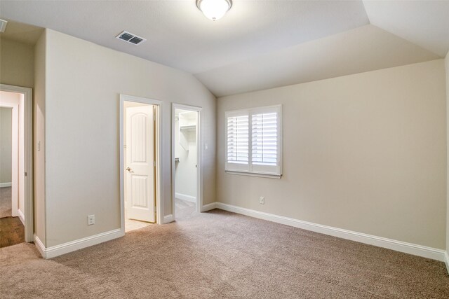 unfurnished bedroom featuring vaulted ceiling, a walk in closet, carpet floors, and a closet