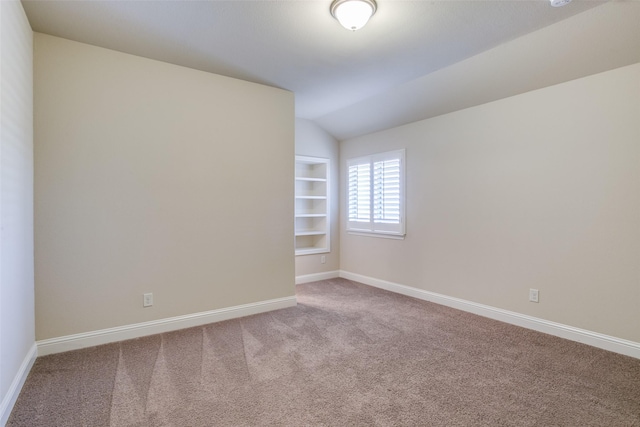 carpeted empty room with vaulted ceiling and built in features