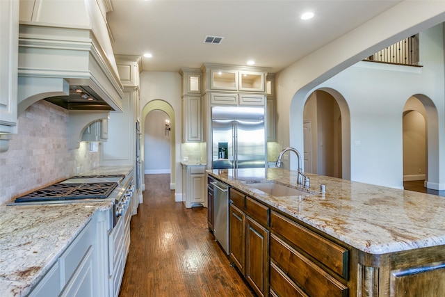 kitchen featuring sink, dark wood-type flooring, a kitchen island with sink, premium appliances, and light stone countertops