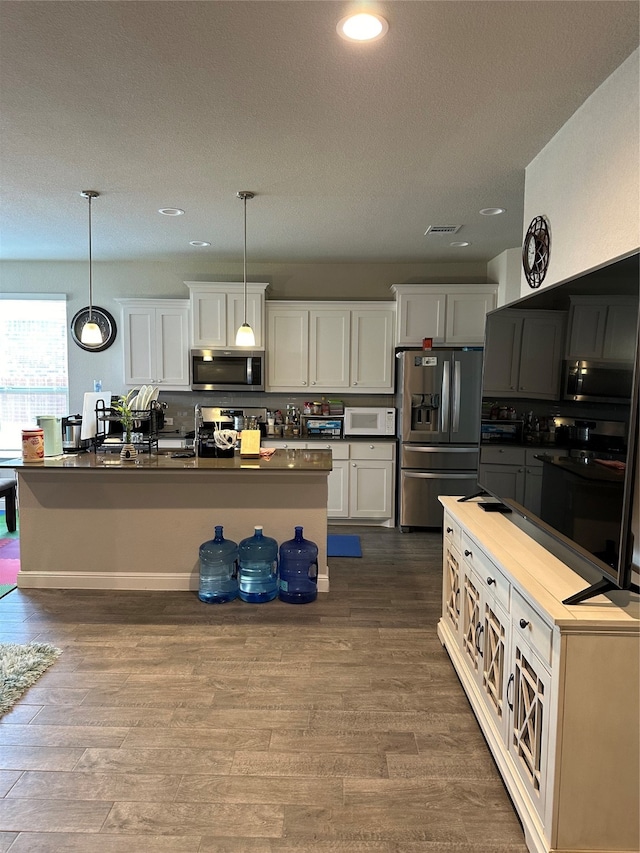 kitchen with pendant lighting, hardwood / wood-style floors, a textured ceiling, appliances with stainless steel finishes, and white cabinets