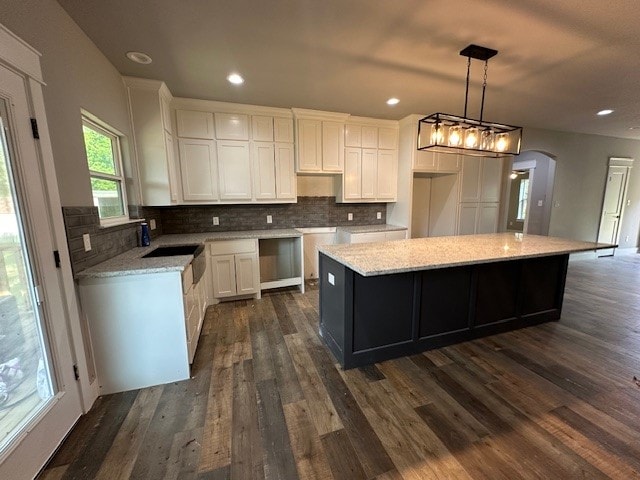 kitchen with white cabinets, hanging light fixtures, a center island, dark wood-type flooring, and tasteful backsplash