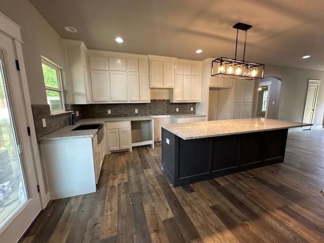 kitchen with dark wood-style flooring, decorative backsplash, a kitchen island, arched walkways, and white cabinets