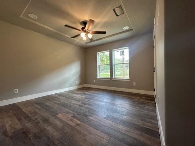 unfurnished room featuring dark wood-type flooring, ceiling fan, baseboards, and a raised ceiling