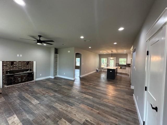 unfurnished living room with baseboards, ceiling fan, recessed lighting, dark wood finished floors, and arched walkways
