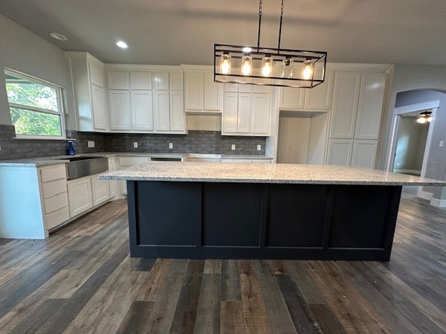 kitchen featuring light stone counters, white cabinetry, dark hardwood / wood-style floors, pendant lighting, and a kitchen island