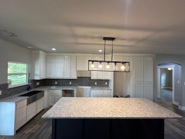 kitchen featuring a center island, decorative backsplash, a sink, arched walkways, and white cabinets
