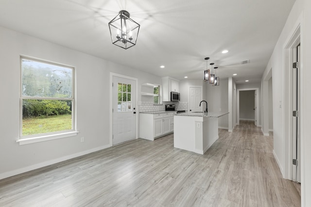 kitchen featuring white cabinets, hanging light fixtures, plenty of natural light, and a center island with sink