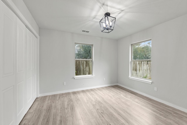 unfurnished bedroom featuring light wood-type flooring, a closet, and a chandelier