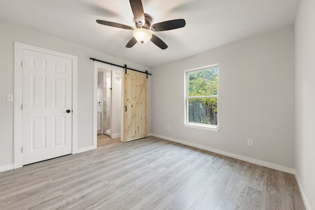 unfurnished bedroom featuring ensuite bath, light hardwood / wood-style flooring, ceiling fan, and a barn door