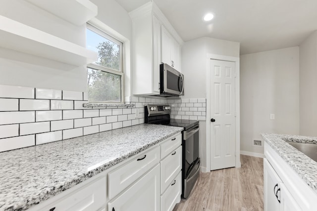 kitchen with light wood-type flooring, light stone countertops, stainless steel appliances, white cabinetry, and tasteful backsplash