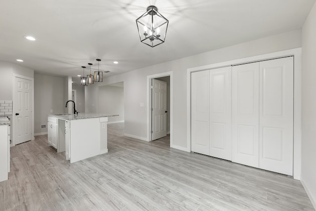 kitchen with a kitchen island with sink, pendant lighting, sink, and light wood-type flooring