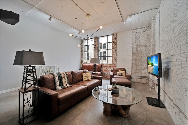 living room with an inviting chandelier, brick wall, rail lighting, and concrete floors