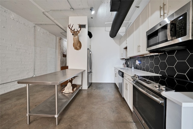 kitchen featuring sink, appliances with stainless steel finishes, white cabinetry, tasteful backsplash, and brick wall