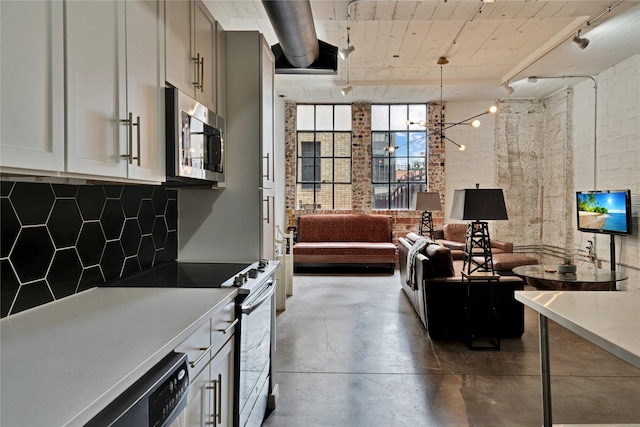 kitchen featuring brick wall, appliances with stainless steel finishes, pendant lighting, a notable chandelier, and track lighting