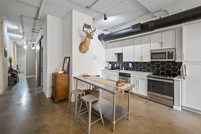 kitchen featuring tasteful backsplash, concrete floors, track lighting, appliances with stainless steel finishes, and white cabinets