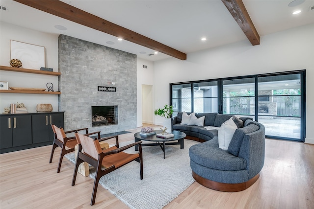 living room featuring beam ceiling, a large fireplace, and light hardwood / wood-style floors