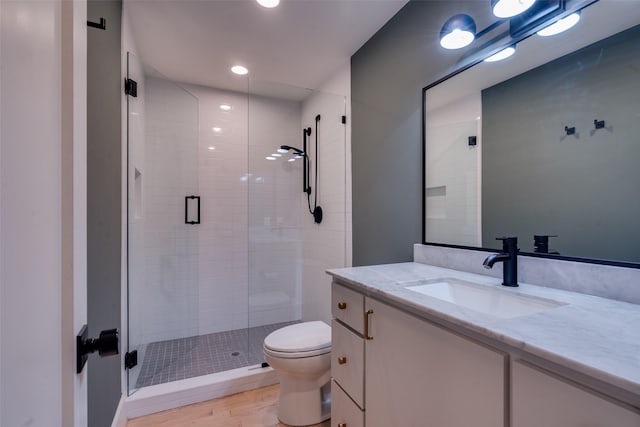 bathroom with toilet, a shower with shower door, hardwood / wood-style floors, and vanity