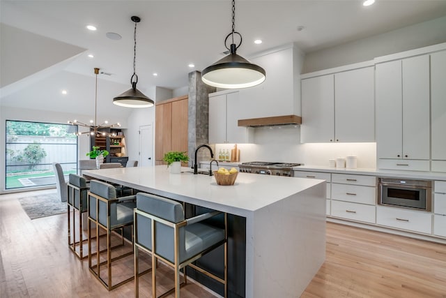 kitchen featuring custom exhaust hood, pendant lighting, white cabinets, and a kitchen island with sink