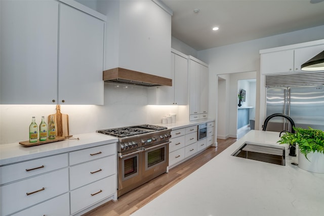 kitchen with light hardwood / wood-style floors, sink, white cabinets, and built in appliances