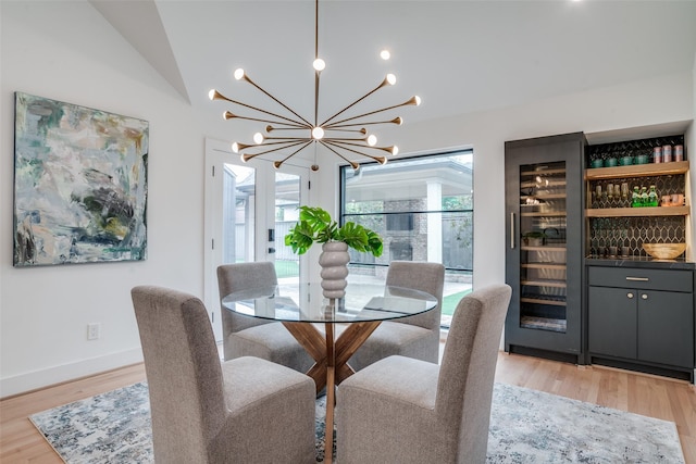 dining room featuring beverage cooler, lofted ceiling, indoor bar, an inviting chandelier, and light hardwood / wood-style floors