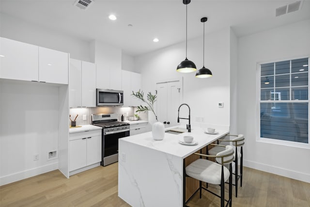 kitchen featuring appliances with stainless steel finishes, hanging light fixtures, light hardwood / wood-style floors, and white cabinetry