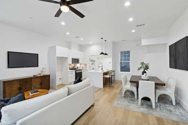 living room with light wood-type flooring, ceiling fan, and sink