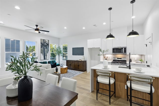 kitchen with light wood-type flooring, pendant lighting, stainless steel appliances, ceiling fan, and white cabinets