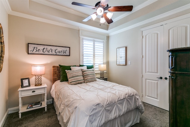 carpeted bedroom with a raised ceiling, ceiling fan, ornamental molding, and a closet