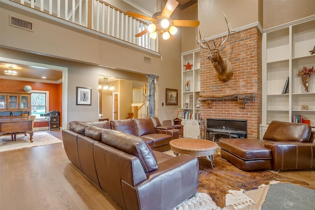 living room with ceiling fan with notable chandelier, crown molding, built in shelves, a fireplace, and wood-type flooring