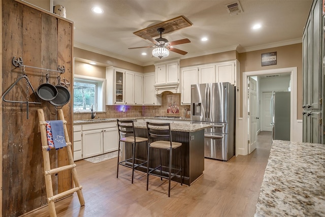 kitchen featuring white cabinetry, a center island, ceiling fan, light stone counters, and appliances with stainless steel finishes