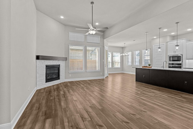 unfurnished living room featuring a brick fireplace, hardwood / wood-style flooring, ceiling fan with notable chandelier, and sink