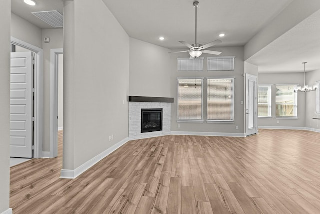 unfurnished living room with a stone fireplace, light hardwood / wood-style flooring, and ceiling fan with notable chandelier