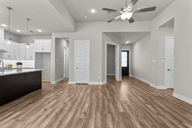 kitchen with sink, light hardwood / wood-style flooring, ceiling fan, hanging light fixtures, and white cabinets