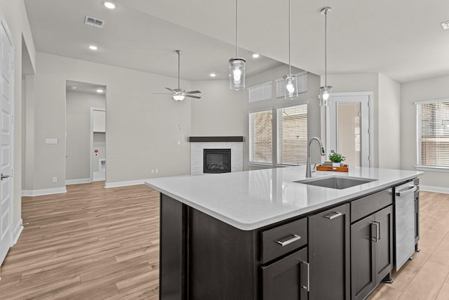 kitchen featuring a stone fireplace, sink, a center island with sink, and light hardwood / wood-style flooring