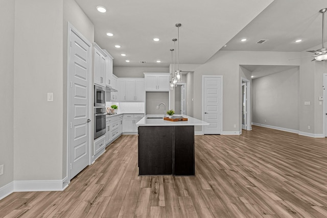 kitchen with sink, ceiling fan, hanging light fixtures, white cabinets, and a center island with sink