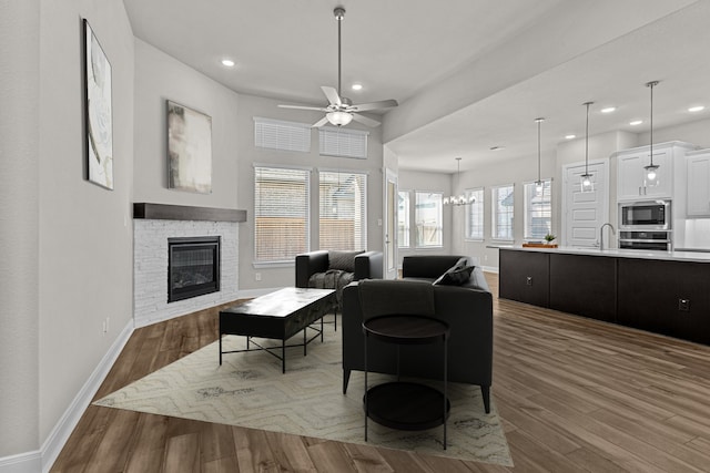 living room with a stone fireplace, dark wood-type flooring, and ceiling fan with notable chandelier